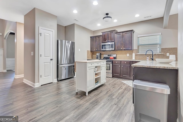 kitchen with arched walkways, light wood finished floors, stainless steel appliances, visible vents, and dark brown cabinetry