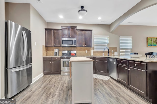 kitchen with stainless steel appliances, backsplash, light wood-style flooring, a kitchen island, and dark brown cabinets