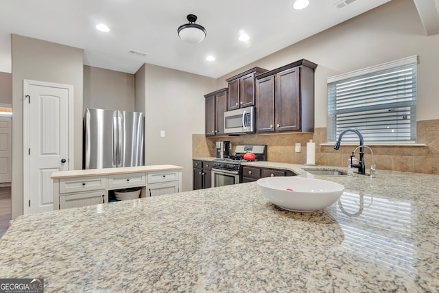 kitchen with backsplash, light stone countertops, sink, stainless steel appliances, and dark brown cabinets