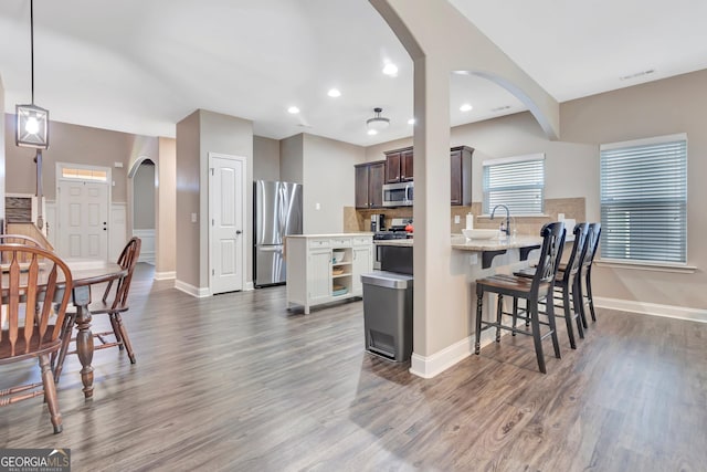 kitchen with appliances with stainless steel finishes, arched walkways, dark brown cabinetry, and wood finished floors