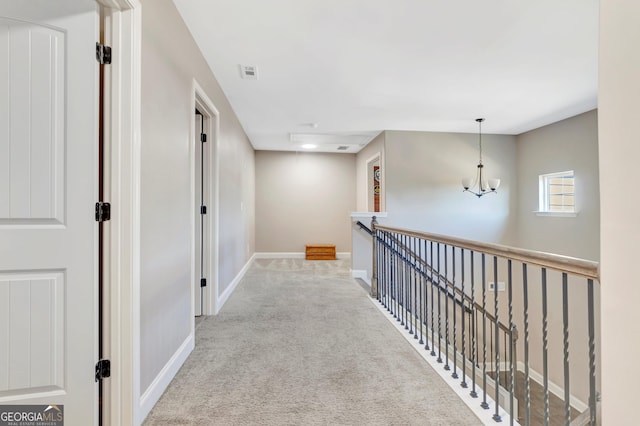 hall with a notable chandelier, light colored carpet, visible vents, an upstairs landing, and baseboards