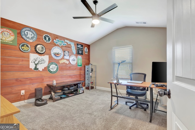 carpeted home office with ceiling fan, wooden walls, and lofted ceiling