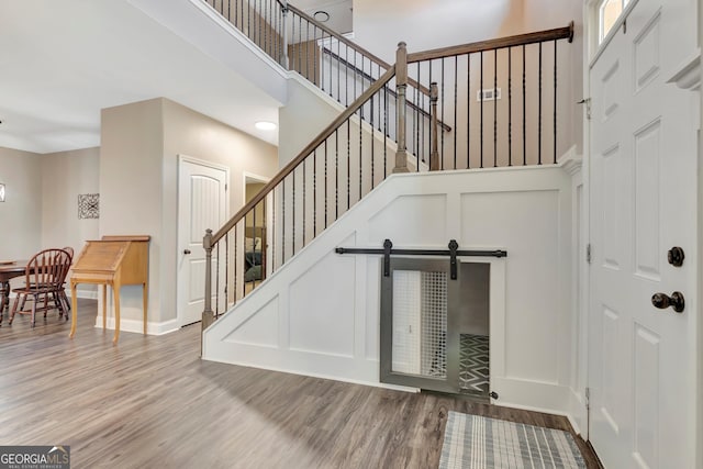 staircase with a towering ceiling, a decorative wall, and wood finished floors