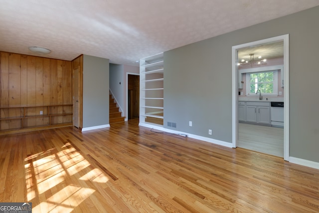 unfurnished living room with an inviting chandelier, light hardwood / wood-style flooring, a textured ceiling, and sink