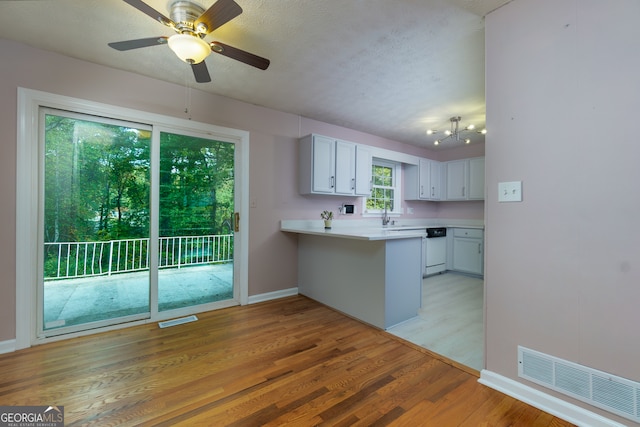 kitchen with dishwasher, light wood-type flooring, a textured ceiling, kitchen peninsula, and white cabinets