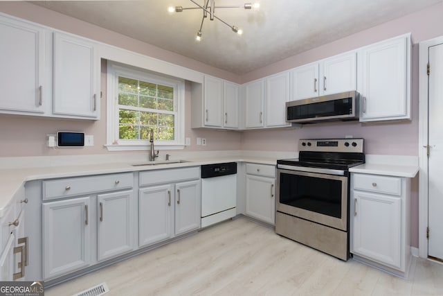 kitchen featuring appliances with stainless steel finishes, an inviting chandelier, white cabinetry, light hardwood / wood-style flooring, and sink