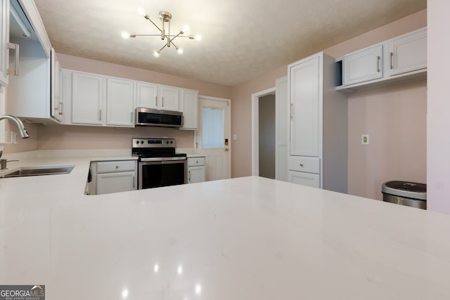 kitchen featuring appliances with stainless steel finishes, sink, a textured ceiling, white cabinets, and an inviting chandelier