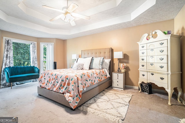 bedroom with ceiling fan, light colored carpet, a textured ceiling, and a tray ceiling