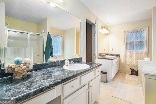 bathroom with tile patterned flooring, a textured ceiling, a shower with door, and vanity