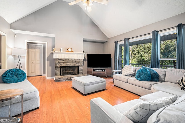 living room featuring hardwood / wood-style floors, high vaulted ceiling, a stone fireplace, and ceiling fan