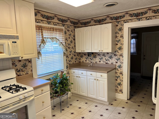 kitchen featuring a textured ceiling, white appliances, and white cabinetry