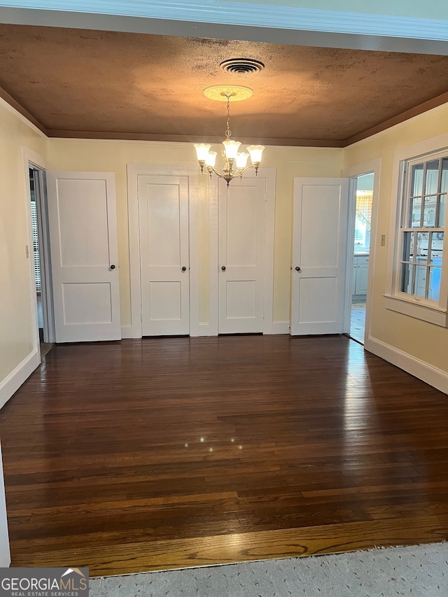 unfurnished dining area featuring a textured ceiling, ornamental molding, an inviting chandelier, and dark wood-type flooring