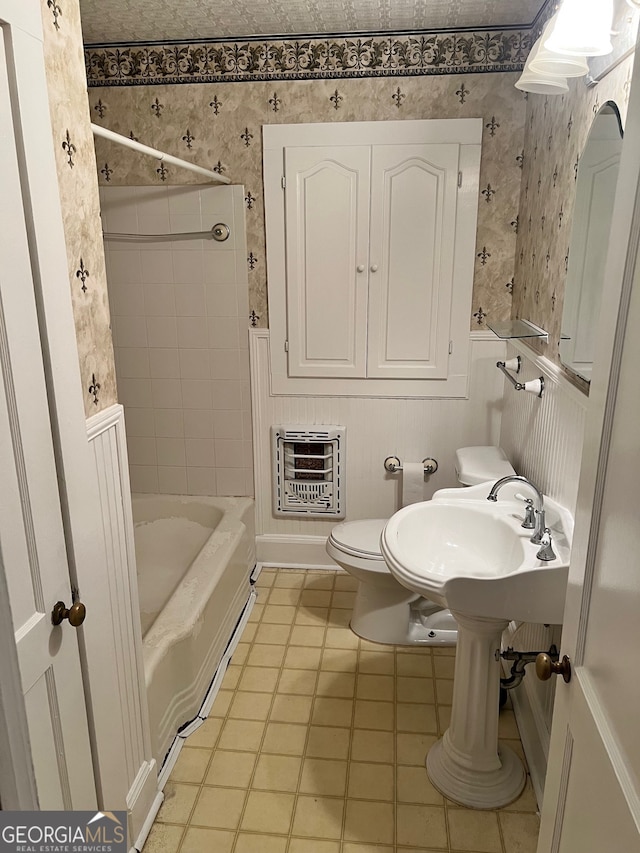 bathroom with heating unit, tiled shower / bath combo, toilet, and tile patterned flooring