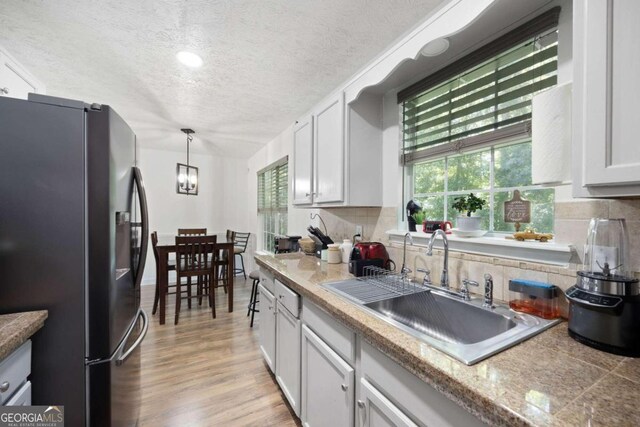 kitchen with black refrigerator with ice dispenser, light hardwood / wood-style flooring, white cabinetry, tasteful backsplash, and hanging light fixtures