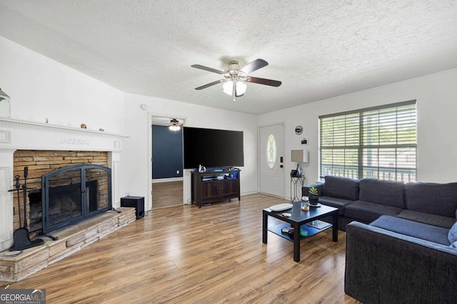 living room with a textured ceiling, ceiling fan, hardwood / wood-style floors, and a stone fireplace