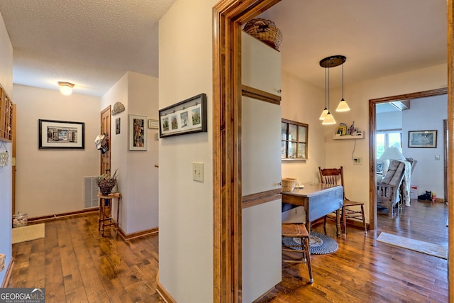 corridor with a textured ceiling and dark hardwood / wood-style flooring