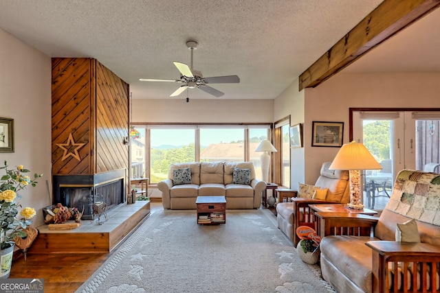 living room with ceiling fan, beamed ceiling, a textured ceiling, and a fireplace