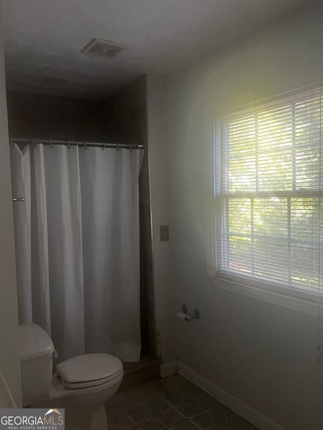 bathroom with toilet, walk in shower, a wealth of natural light, and tile patterned flooring