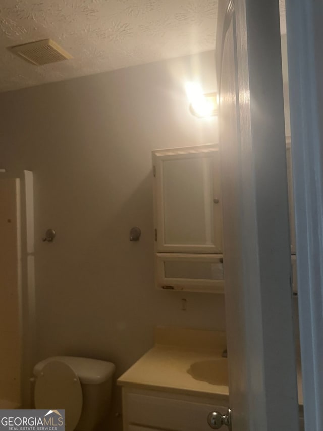 bathroom featuring vanity, a textured ceiling, and toilet