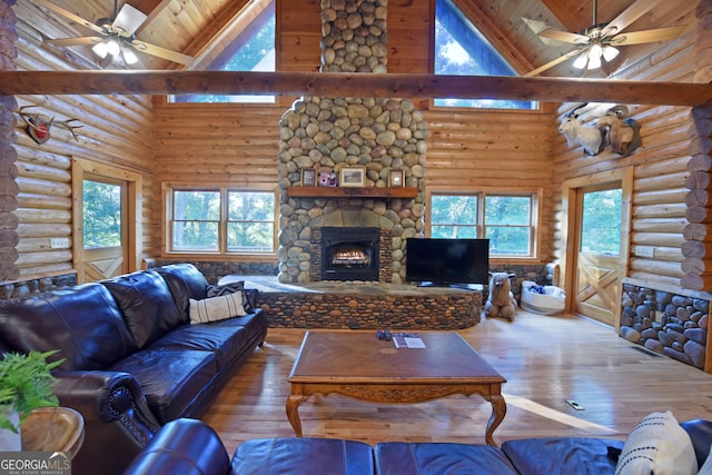 living room featuring a healthy amount of sunlight, high vaulted ceiling, hardwood / wood-style flooring, and a stone fireplace