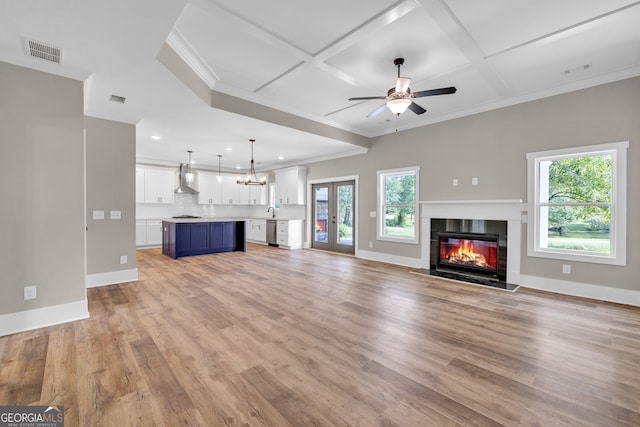 unfurnished living room featuring ceiling fan with notable chandelier, crown molding, coffered ceiling, and light hardwood / wood-style floors