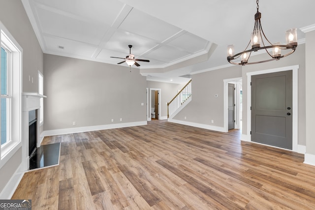 unfurnished living room featuring ceiling fan with notable chandelier, coffered ceiling, plenty of natural light, and light hardwood / wood-style floors