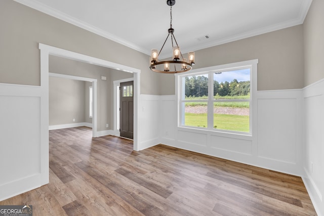 unfurnished dining area with an inviting chandelier, crown molding, and light hardwood / wood-style flooring