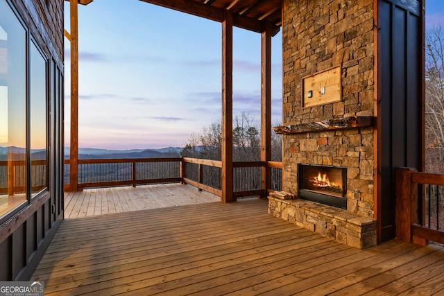 deck at dusk featuring a mountain view and an outdoor stone fireplace