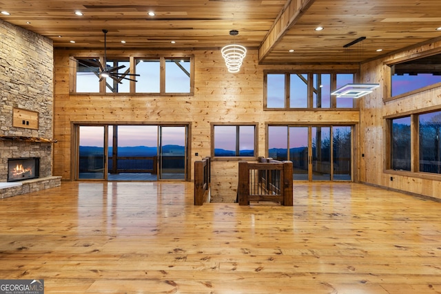 living room featuring a stone fireplace, light wood-type flooring, ceiling fan, wooden ceiling, and a towering ceiling