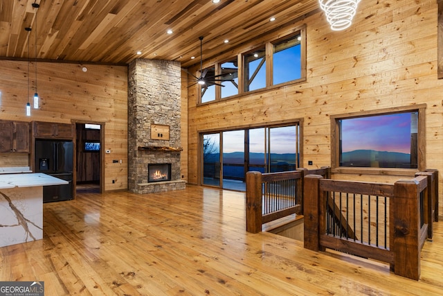 living room with wood ceiling, light hardwood / wood-style flooring, ceiling fan, a stone fireplace, and wood walls