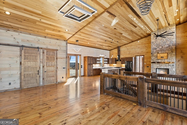 living room featuring high vaulted ceiling, light wood-type flooring, wooden ceiling, wooden walls, and a fireplace