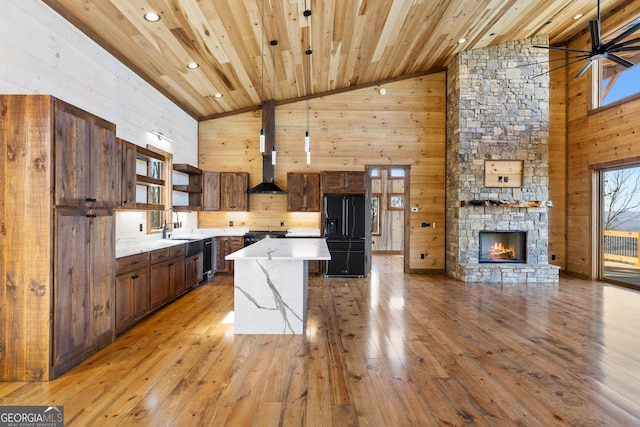 kitchen featuring a center island, light hardwood / wood-style floors, wood ceiling, wall chimney range hood, and black refrigerator with ice dispenser