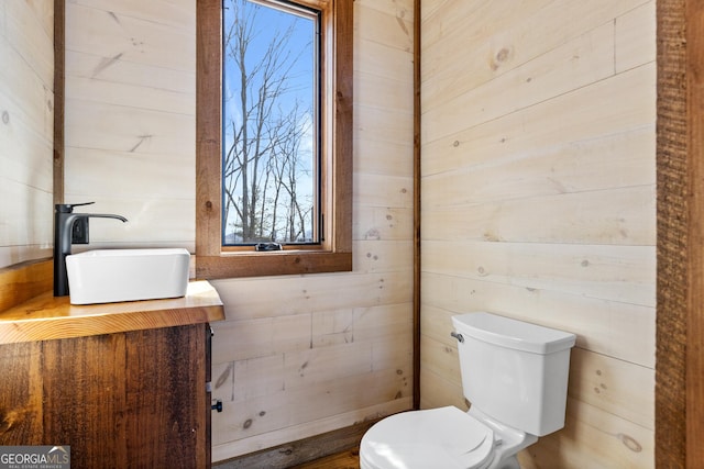 bathroom featuring sink, wooden walls, and toilet