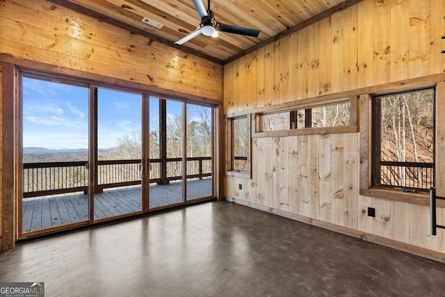 empty room featuring a mountain view, wooden ceiling, ceiling fan, and wood walls