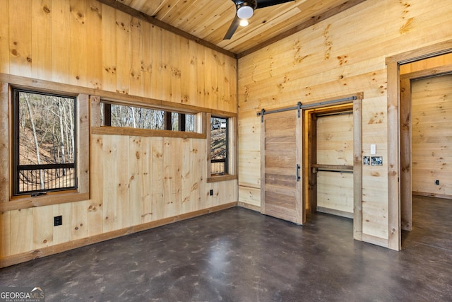 spare room with a towering ceiling, wooden walls, ceiling fan, wood ceiling, and a barn door