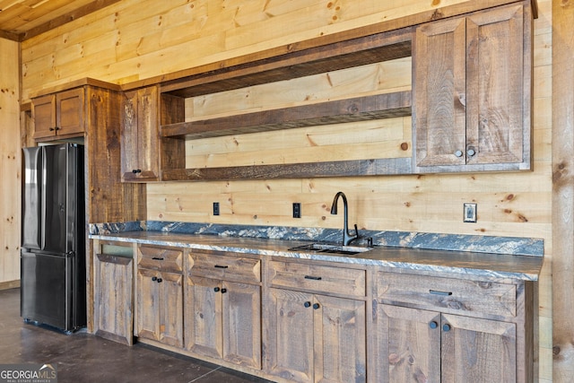 kitchen with black fridge, sink, and wood walls