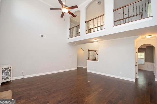 unfurnished living room with a towering ceiling, dark hardwood / wood-style floors, ceiling fan, and ornamental molding