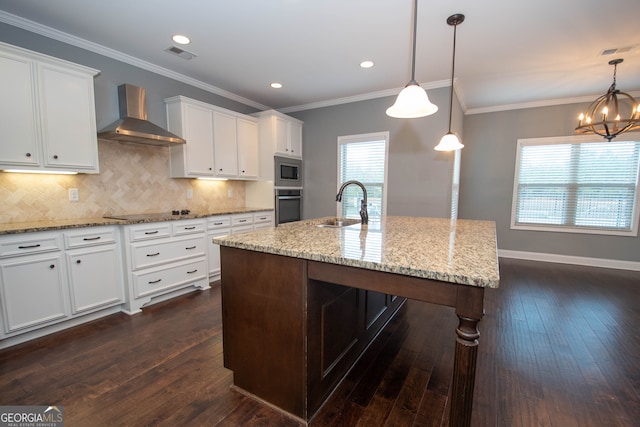 kitchen featuring wall chimney exhaust hood, a healthy amount of sunlight, dark hardwood / wood-style floors, a center island with sink, and appliances with stainless steel finishes