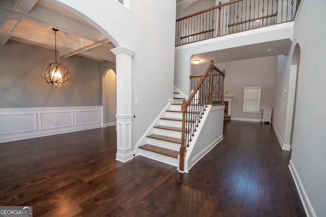 stairs with beamed ceiling, decorative columns, a towering ceiling, a chandelier, and hardwood / wood-style flooring