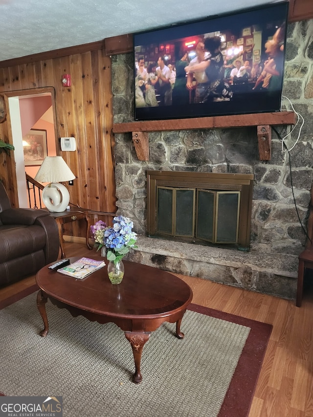 living room with hardwood / wood-style floors, a stone fireplace, a textured ceiling, and wooden walls