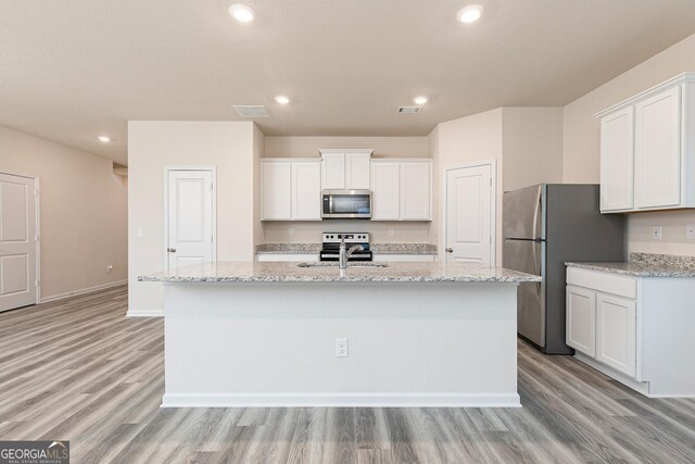 kitchen with light wood-type flooring, appliances with stainless steel finishes, a center island with sink, and white cabinetry