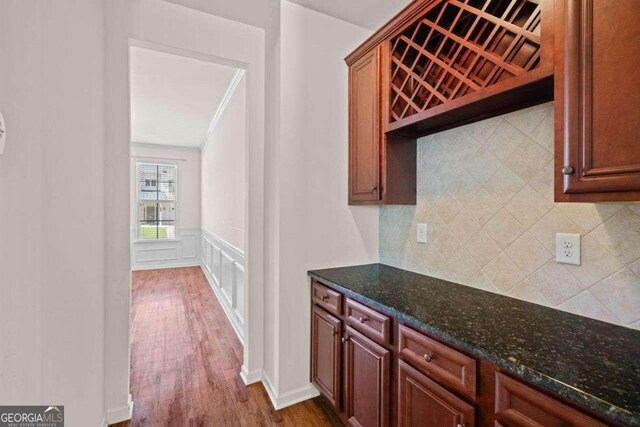 bar featuring hardwood / wood-style floors, dark stone countertops, decorative backsplash, and ornamental molding