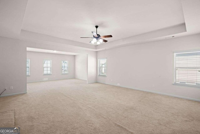 carpeted empty room with a wealth of natural light, ceiling fan, and a tray ceiling