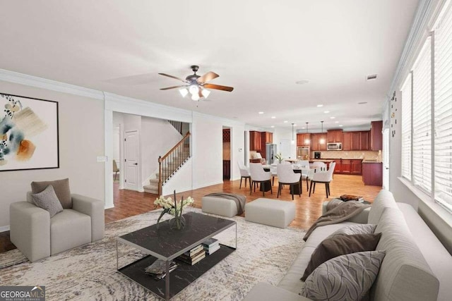 living room featuring a healthy amount of sunlight, ceiling fan, ornamental molding, and light wood-type flooring