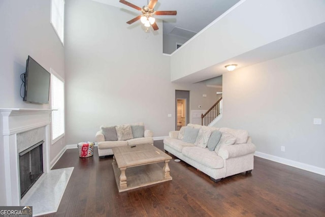 living room with a fireplace, ceiling fan, a towering ceiling, and dark hardwood / wood-style floors