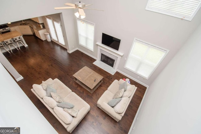 living room with ceiling fan, a high end fireplace, a towering ceiling, and wood-type flooring