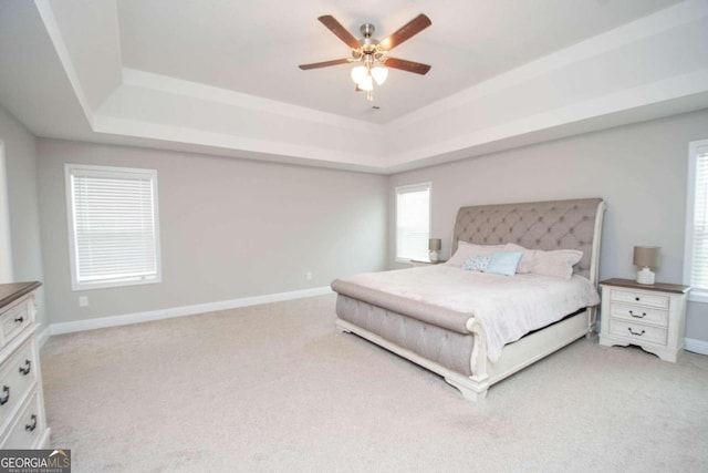 carpeted bedroom with ceiling fan and a tray ceiling