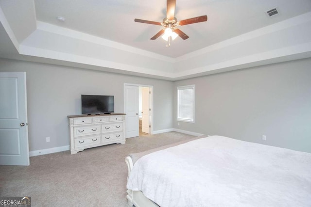 bedroom featuring ceiling fan, a raised ceiling, light carpet, and ensuite bathroom