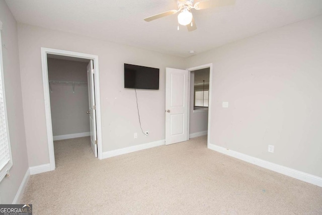 unfurnished bedroom with a walk in closet, light carpet, a closet, and ceiling fan