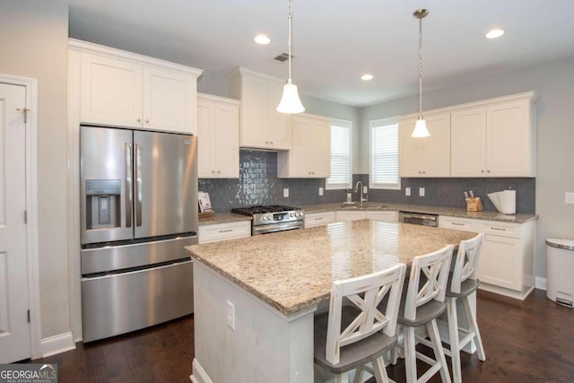 kitchen with appliances with stainless steel finishes, decorative light fixtures, decorative backsplash, a kitchen island, and dark wood-type flooring